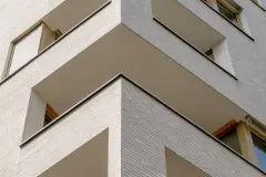 Stadt Carre residential and commercial complex features a facade of clay brick slips and textured, brushed render, both in a light sandy colour.