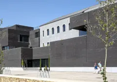 A view of the Trofa Town Hall with the original building visible surrounded by the new rectilinear volumes clad in dark bricks.